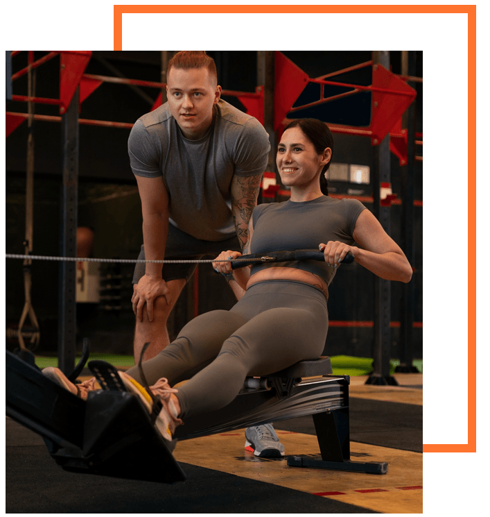 Personal trainer assisting client with rowing machine exercise, demonstrating tailored fitness program.