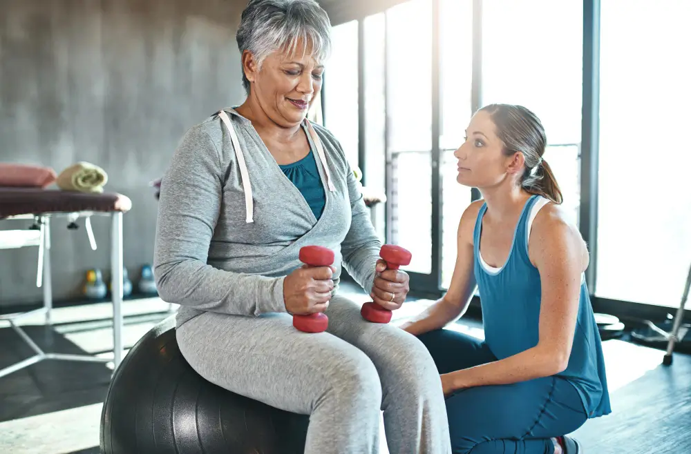 Woman receiving personal training with dumbbells on exercise ball.