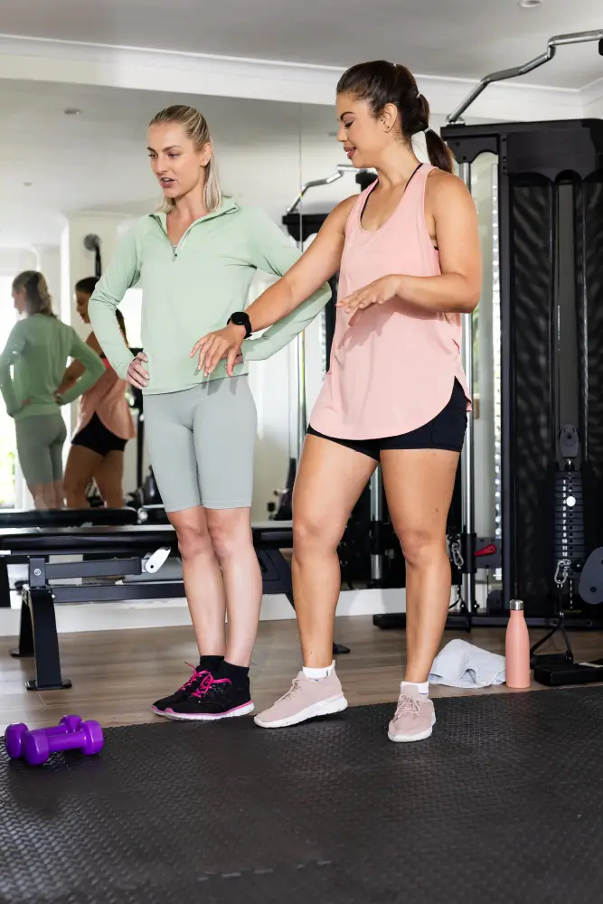 Personal trainer coaching client with posture assessment and exercise guidance in a fitness studio.