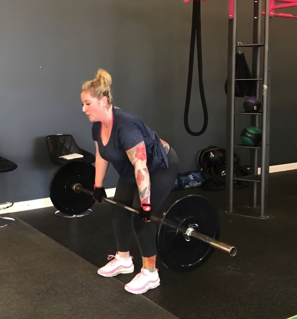 A woman in athletic wear performing a barbell deadlift exercise inside a fitness studio.