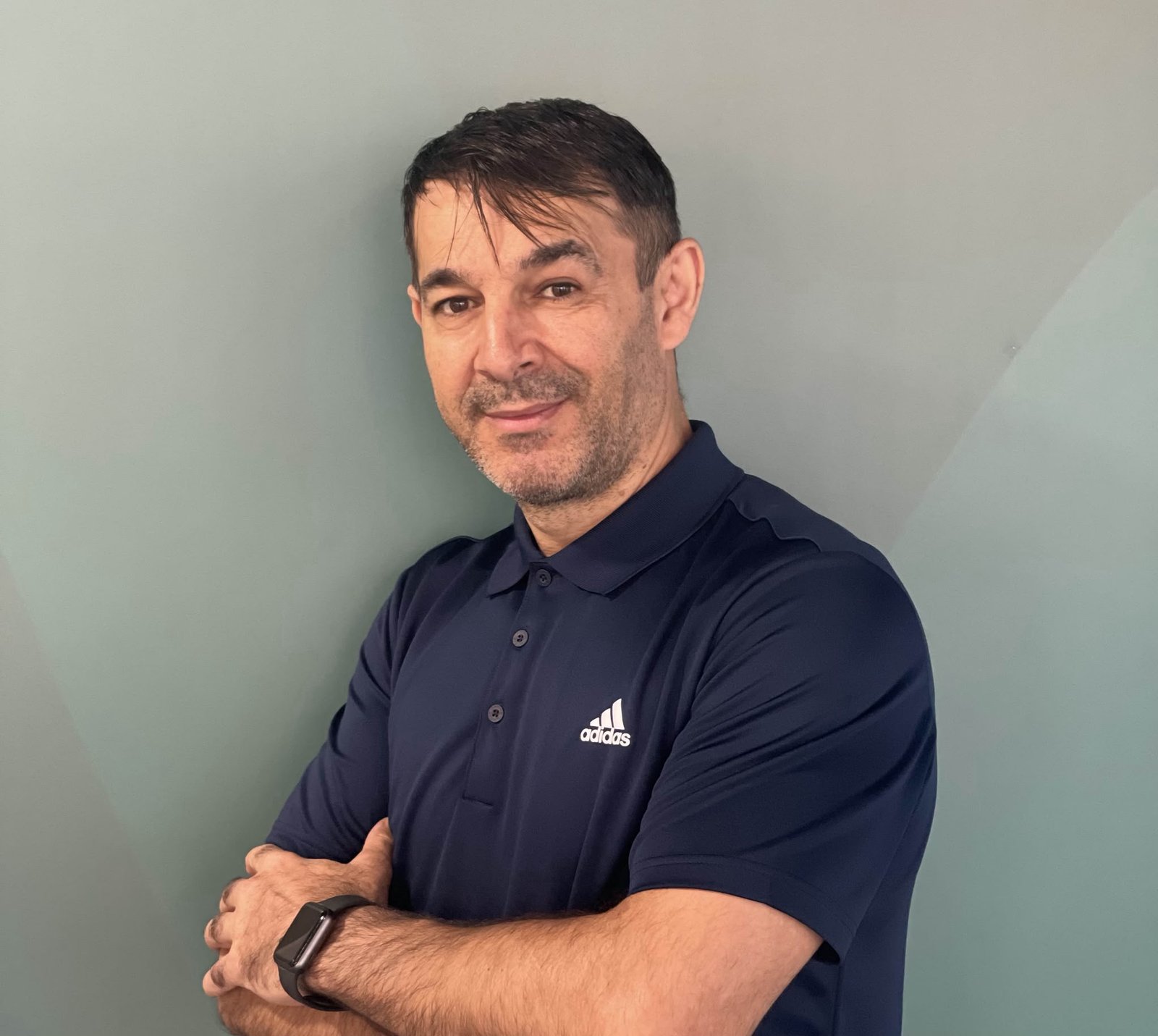 Male personal trainer in a navy polo shirt smiling with arms crossed.