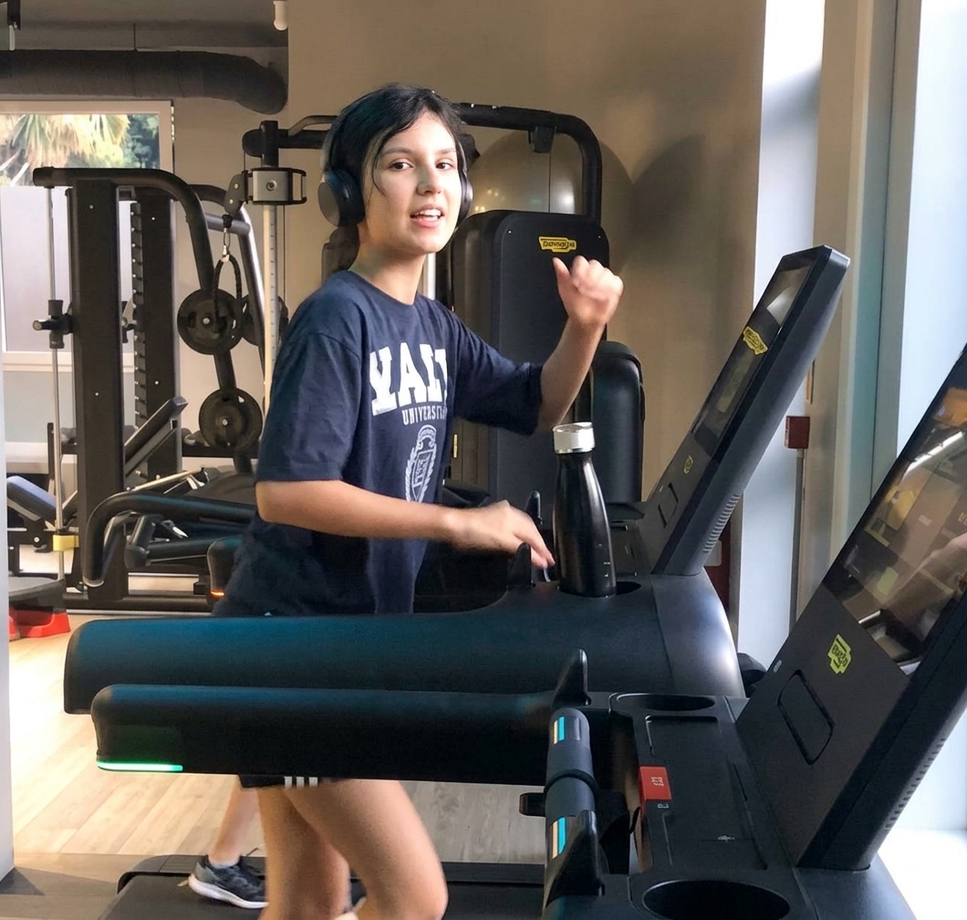Young person wearing over-ear headphones walking on a treadmill in a gym.