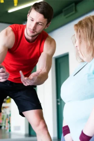 grid-1 Male personal trainer in a red tank top gesturing and encouraging a female client during a personal training session in a gym studio.