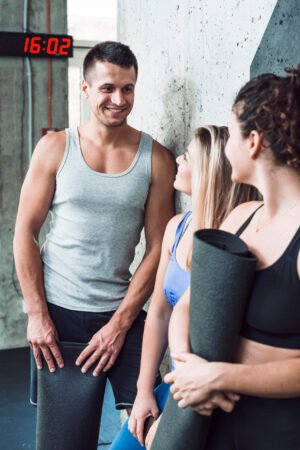 group-happy-people-with-exercise-mat-gym Group of happy fitness clients holding rolled-up exercise mats inside a gym.
